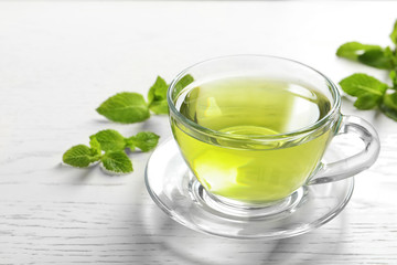 Tasse avec thé à la menthe aromatique chaud et feuilles fraîches sur table