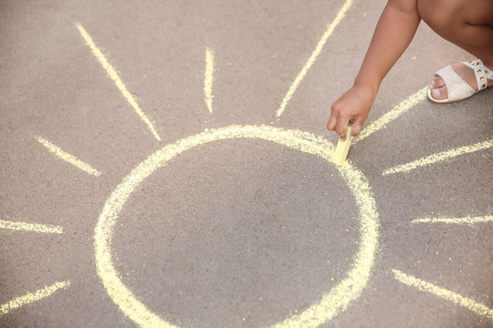 Little child drawing sun with chalk on asphalt