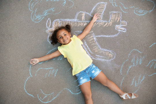 Little African-American Child Lying Near Chalk Drawing Of Airplane On Asphalt, Top View