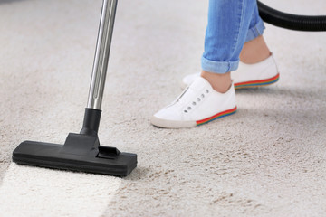 Woman removing dirt from carpet with vacuum cleaner indoors, closeup
