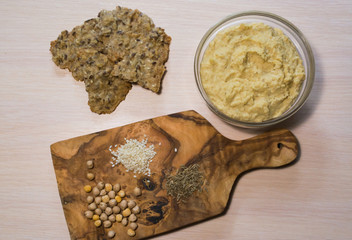 Hummus in a glass bowl with bread and chickpeas, sesame and cumin on the board