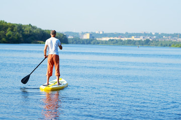 Man sails on a SUP board in large river on the cityscape background
