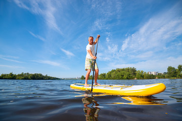 Joyful man sails on a SUP board in large river