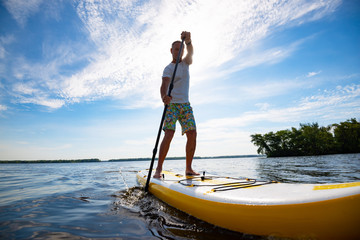 Fototapeta na wymiar Joyful man sails on a SUP board in large river