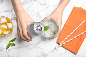 Woman pouring drink from tin can into glass at table, top view