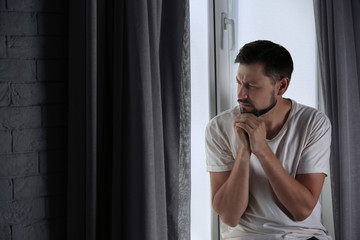 Lonely depressed man near window at home