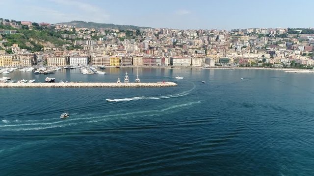 Aerial flight towards Naples Italy approaching from sea side showing marin on left and city on right side also showing some motorboats moving away from marina 4k high resolution quality footage