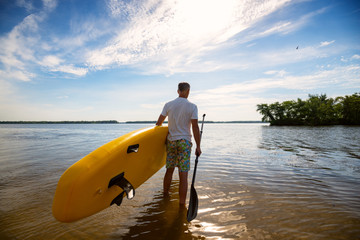 Man is standing with a SUP board and a paddle in his hands