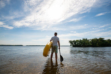 Man walks along the beach with a SUP board and a paddle