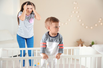 Cute baby boy in crib and young mother suffering from postnatal depression on blurred background