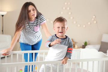 Crying baby boy in crib and young mother suffering from postnatal depression at home