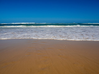 Beautiful empty paradise beach at the ocean with turquoise water, waves and yellow sand