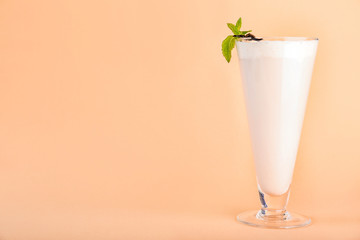 Glass with vanilla milk shake on color background