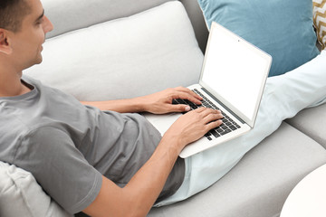 Naklejka premium Man in casual clothes using laptop on sofa at home