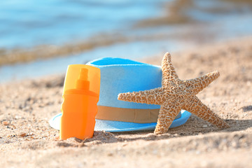 Starfish, bottle with sunscreen and hat on sand near sea. Beach object