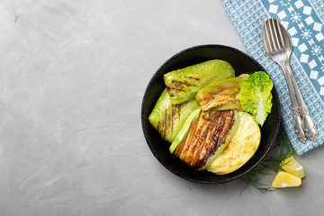 Grilled slices zucchini in a rustic iron pan on a gray stone background. Top view.