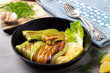 Grilled slices zucchini in a rustic iron pan on a gray stone background