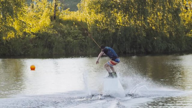 Wakeboarder ride on cable wakeboard in park, outdoor extreme slow motion on water, surfing athlete on water doing boardslide, noseslide or tailslide 180 out, backside bluntslide