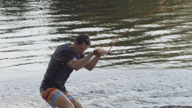 Wakeboarder ride on cable wakeboard in park, outdoor extreme slow motion on water, surfing athlete on water doing boardslide, noseslide or tailslide 180 out, backside bluntslide