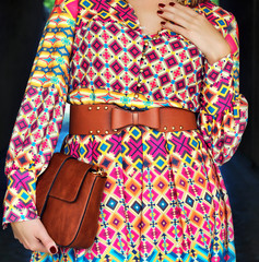 Young beautiful stylish woman walking in street in printed dress brown belt with bow holding brown leather purse in hands. Elegant Lady style