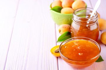 Apricot jam in glass bowl and fresh apricots on light purple wooden background