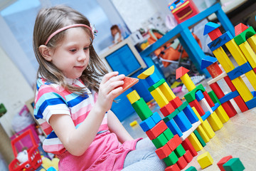 girl playing with wooden toy blocks indoors