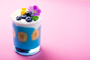 Tropical smoothie dessert with fruits, berries, nuts and flowers on pink background. Exotic healthy smoothie. Healthy breakfast, vegetarian food concept. Copy space