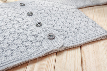 knitted baby jacket gray on a wooden light background, close-up