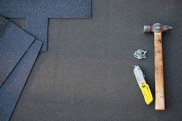 Close up view on unfinished asphalt roofing shingles background with hammer and nails. Installation...