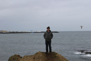Young male 20-25 embracing the nature of Iceland in dramatic photos off of the ocean. Very grey and depressing skies