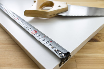 Wooden background with a handsaw and tape ruler lying on white panel