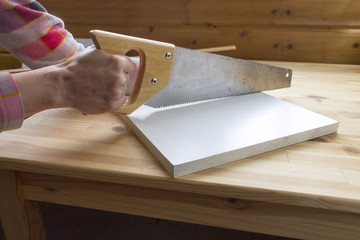 Cropped hands of a carpenter sawing white wooden panel