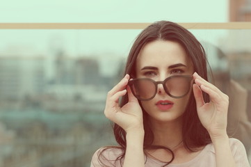 A long-haired young brunette woman plays with sunglasses