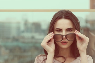 A long-haired young brunette woman plays with sunglasses