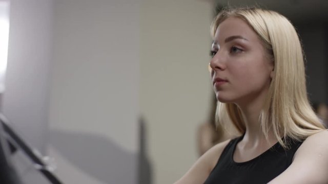 blonde girl turns the pedals on an exercise bike when the coach comes up and asks out how she's doing in new gym