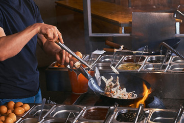 Cooking process in an Asian restaurant. Cook is stirring vegetables in wok.