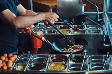 Cooking process in an Asian restaurant. Cook is stirring vegetables in wok.