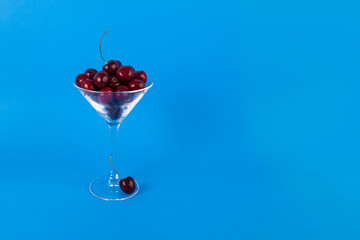 Martini glass of cherries framed left on a solid blue background