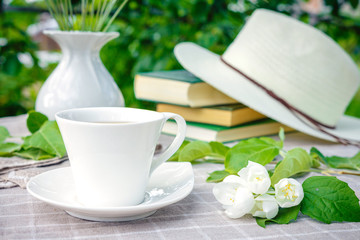 cup with tea, a laptop, a computer, a bookshine table in the garden on a summer morning, a place to work, a concept of freelancing