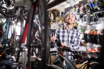 Fototapeta na wymiar admiring man in helmet chooses for himself sports bike in bicycle shop