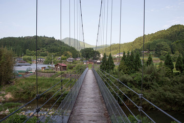 Narrow suspension bridge leading to small Japanese village with Soni Kogen visible in the background