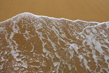 Wave of the sea with white foam against the background of a sandy beach. View from above