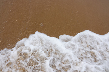 Wave of the sea with white foam against the background of a sandy beach. View from above