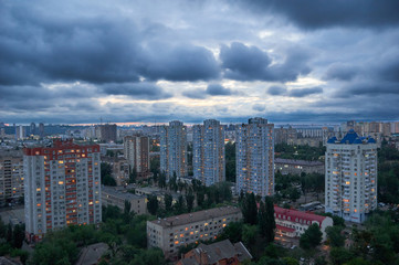 Fototapeta premium Beautiful night cityscape with cloudy sky/Aerial view of Kyiv's city residential district after the sun has set.Dark rainy clouds in the blue sky over the city.Urban night cityscape