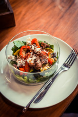 Glass bowl of healthy roasted vegetables salad on a wooden table. Low key food photography, warm toned filter