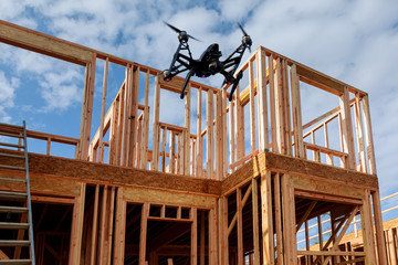 Black drone quadcopter with camera flying over residential construction home framing against