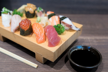 Close-up sushi and sashimi mixed on wooden plate on black wooden table. Japanese food.