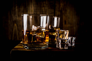 Two whiskey shot glasses on dark wooden background, with ice cubes, copy space