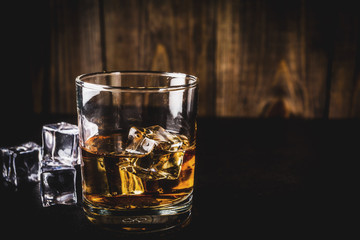 Two whiskey shot glasses on dark wooden background, with ice cubes, copy space
