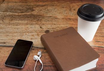 Physical Bible and a Smart Phone with Earphones on a Wood Table